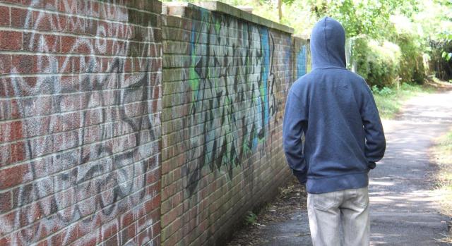 Medidas urgentes para la protección de menas: el RDL 2/2025. Imagen de un joven de espaldas al lado de un muro lleno de grafitis