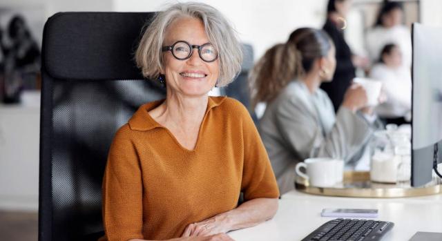 Publicada la norma que mejora la compatibilidad de la pensión de jubilación con el trabajo. Imagen de un retrato de una alegre empresaria senior sentada en el escritorio de la oficina