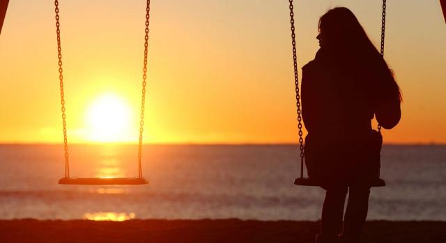 Tiene derecho a pensión de viudedad la mujer de un trabajador fallecido durante una excedencia de 3 meses. Imagen de una mujer columpiandose en un columpio de dos, sola, mirando el atardecer sobre el mar